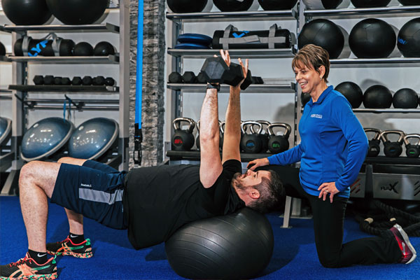 Personal Trainer helping man with weight training exercise on a yoga ball.