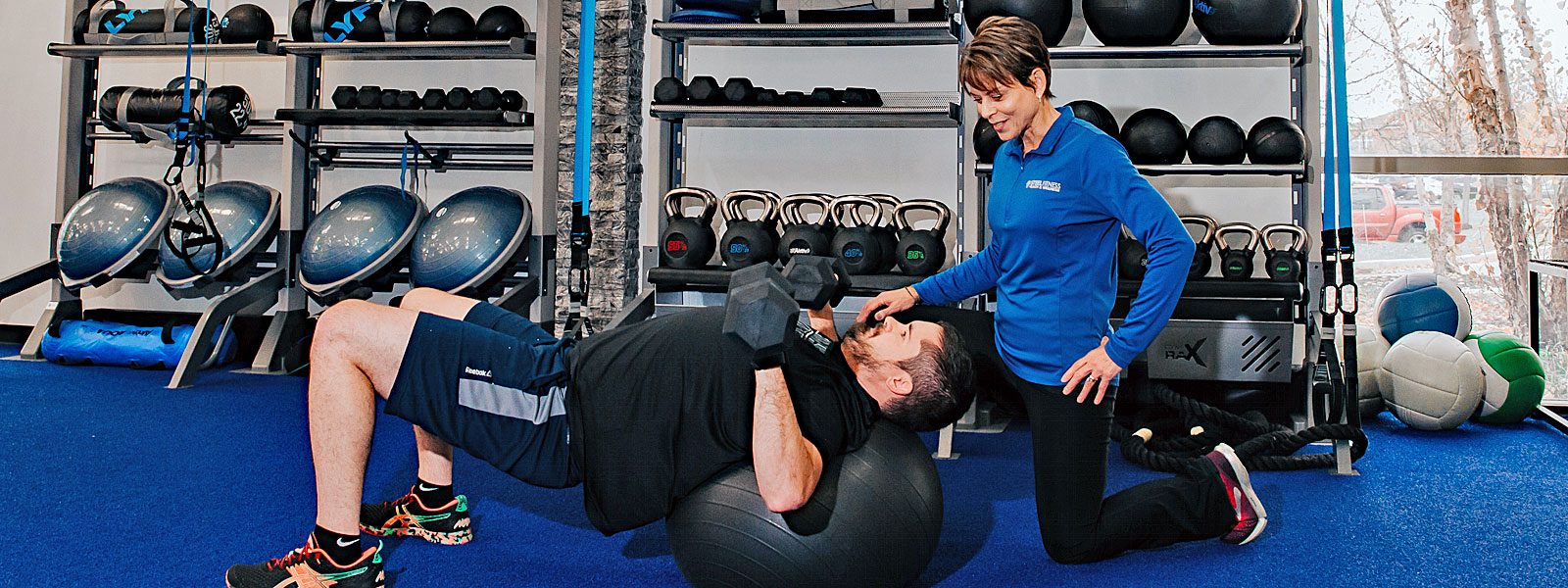 Man lifting weights with a yoga ball working out with a personal trainer.